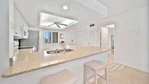Una cucina moderna con mobili bianchi, un piano di lavoro in granito e una ventola a soffitto.