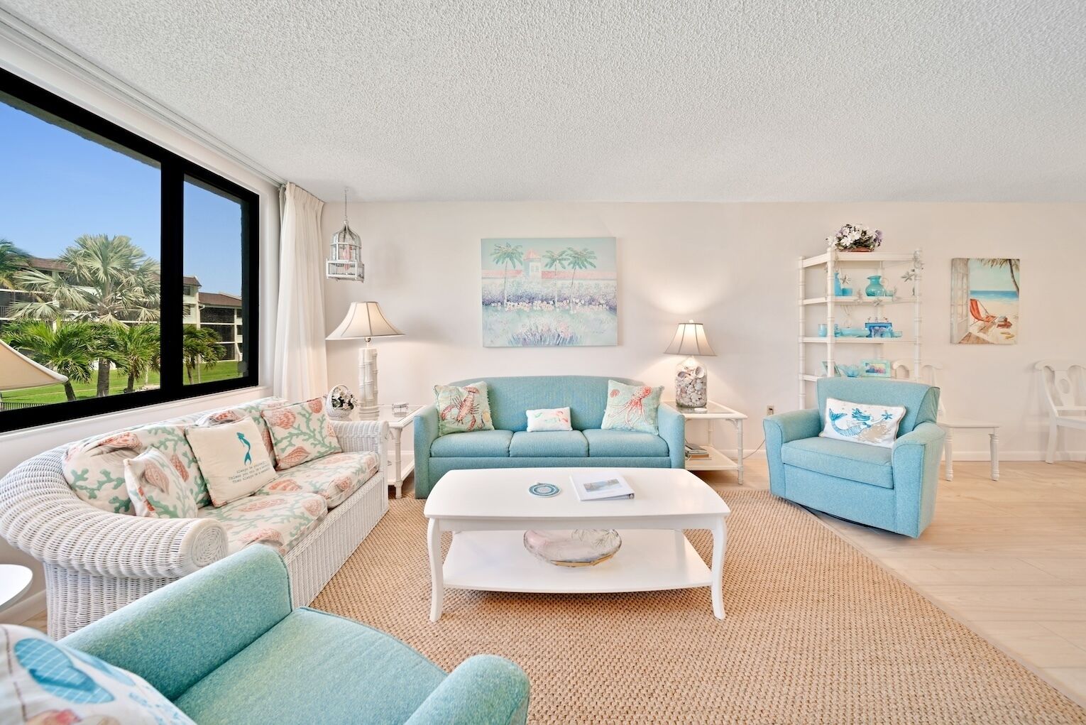 A living room with a large window, a light blue sofa, a white coffee table, and a white armchair.