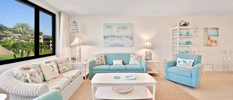 A living room with a large window, a light blue sofa, a white coffee table, and a white armchair.