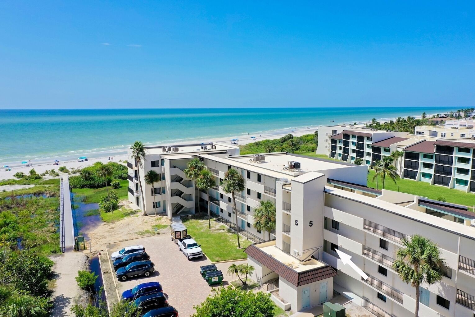 Ein Strandhotel mit mehreren Etagen, einem Parkplatz und Blick aufs Meer.