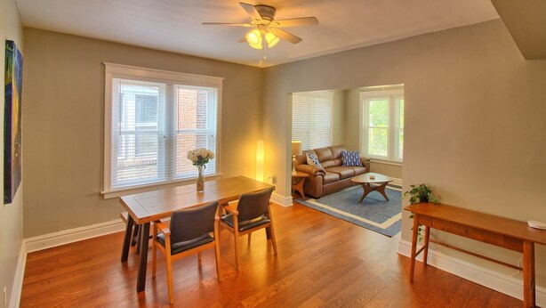 A spacious living room with a wooden floor, a ceiling fan, a dining table with chairs, a sofa, and a coffee table. - Cafe Terrace at TG Park | Fenced Backyard+W/D (Saint Louis)