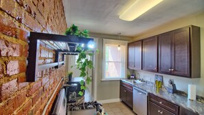 A kitchen with brick walls, a gas stove, a sink, and wooden cabinets. - Cafe Terrace at TG Park | Fenced Backyard+W/D (Saint Louis)