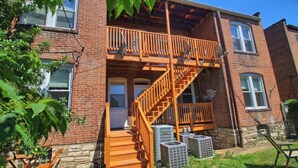A two-story brick building with a wooden balcony and a fire escape. - Cafe Terrace at TG Park | Fenced Backyard+W/D (Saint Louis)