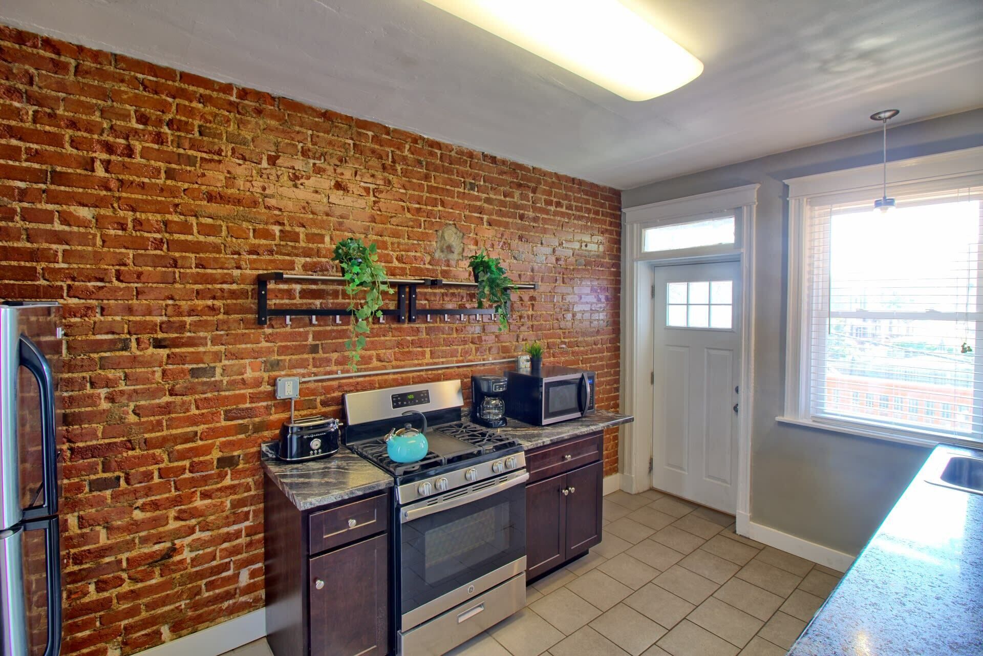 A kitchen with brick walls, a microwave, a stove, and a coffee maker.