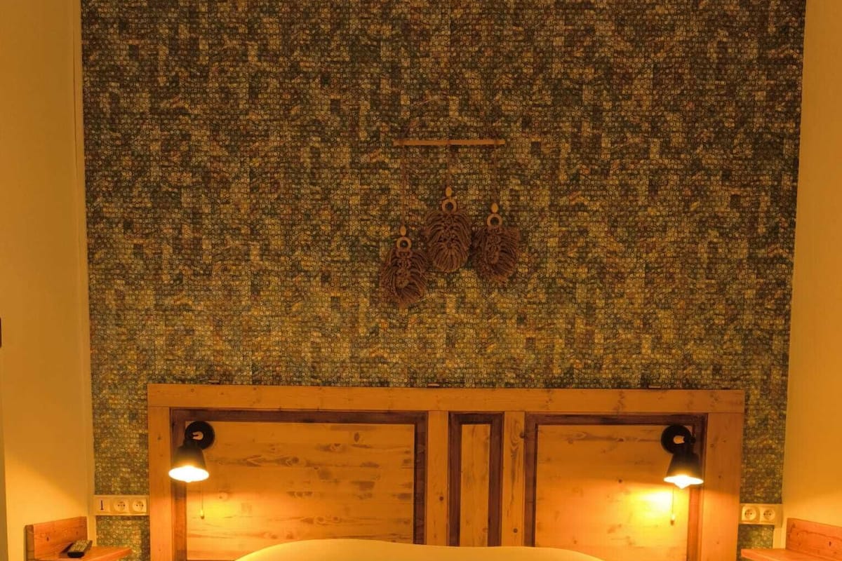 Een netjes opgemaakt bed met twee kussens en opgevouwen handdoeken, een houten hoofdbord en twee bedlampjes.