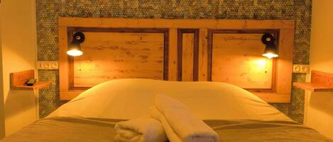 A neatly made bed with two pillows and folded towels, a wooden headboard, and two bedside lamps.