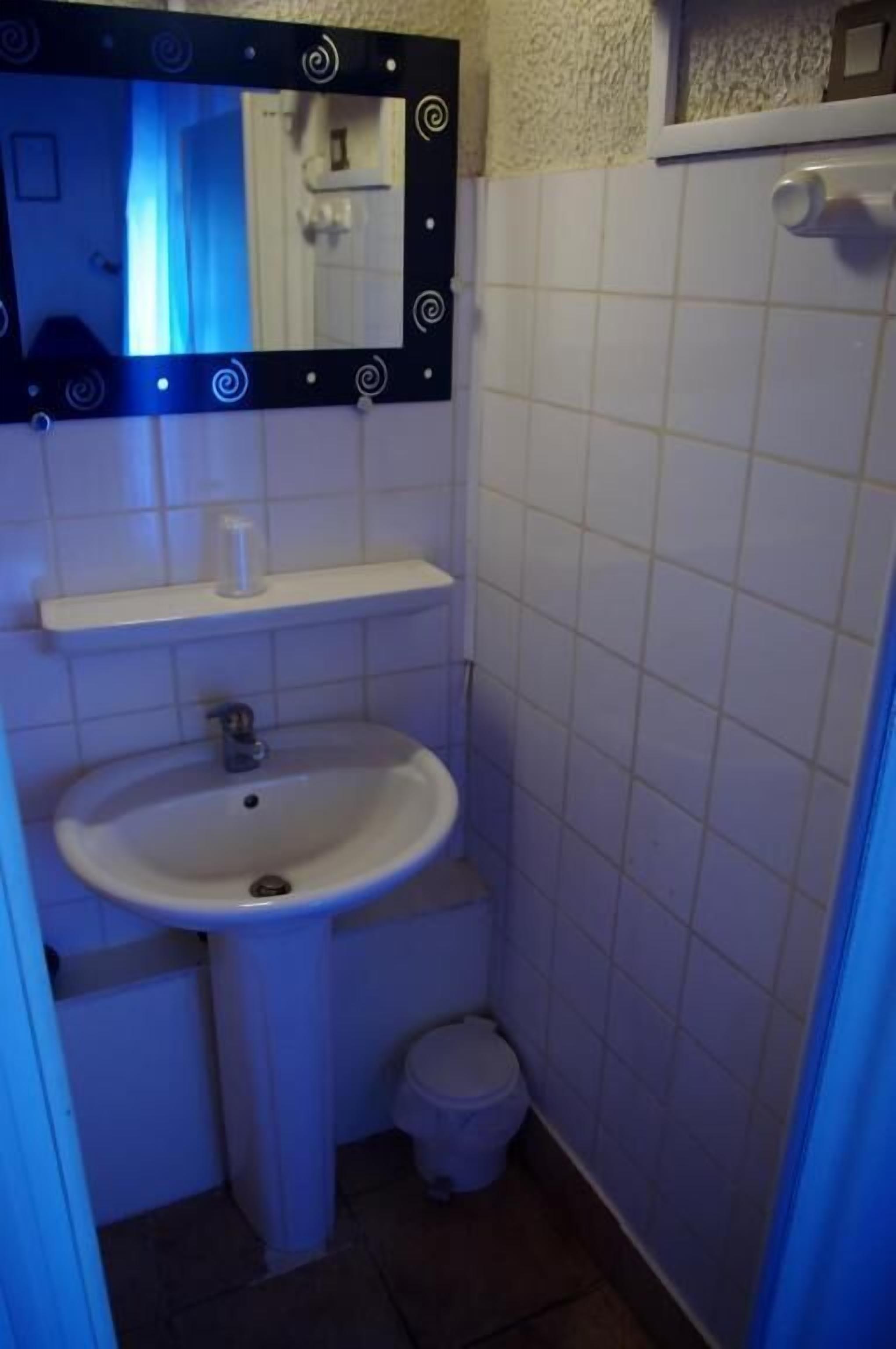 Ein kleines Badezimmer mit einem weißen Waschbecken, einer Toilette und einem Spiegel mit schwarzem Rahmen.