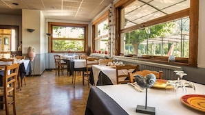 Un restaurant avec des tables et des chaises en bois, de grandes fenêtres donnant sur un paysage verdoyant et un décor intérieur de style rustique.