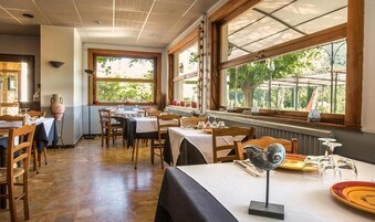 Un restaurante con mesas y sillas de madera, ventanas amplias con vistas a la vegetación y una decoración rústica.