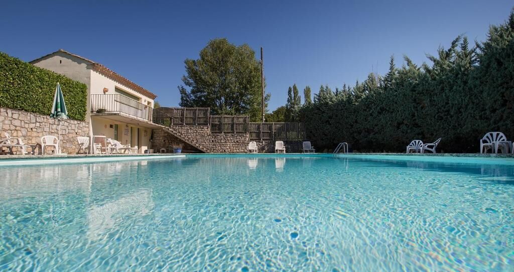 A clear swimming pool with lounge chairs and a stone wall.