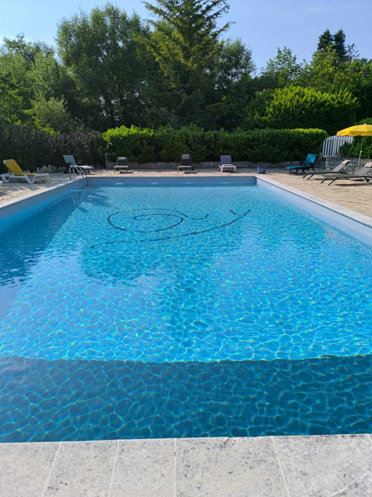 A rectangular swimming pool with clear blue water, surrounded by lounge chairs and a stone deck.