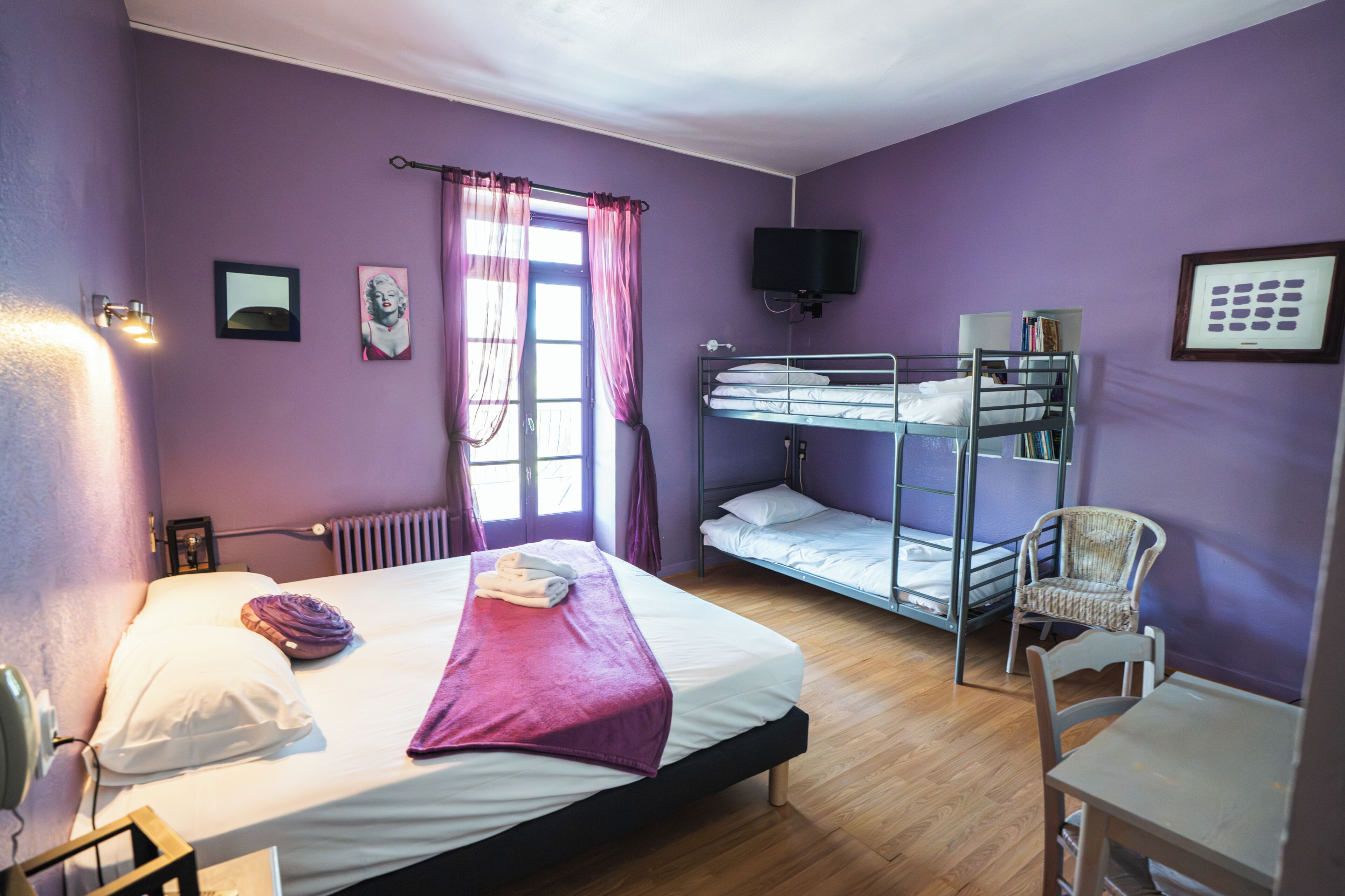 A room with a single bed, a bunk bed, a chair, a television, and a window with curtains.