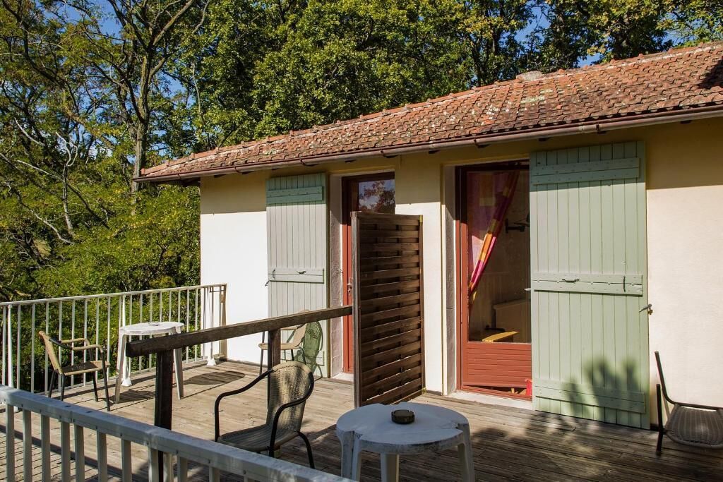 Een klein gebouw met een pannendak, een balkon met een leuning en een tafel met stoelen op het terras.