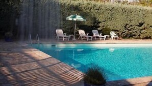 Une piscine agrémentée d’une cascade, entourée de chaises longues et d’une plante en pot.