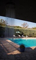 Una piscina con cascada, rodeada de sillas de descanso y una planta en maceta.