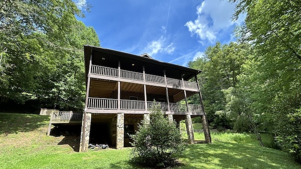 A two-story wooden cabin with a balcony, surrounded by lush greenery. - Dream on a Stream Log Cabin Lodge That Has It All! (Almond)
