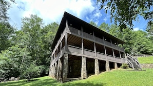 A two-story wooden structure with stone pillars, a balcony, and a staircase leading to the upper level. - Dream on a Stream Log Cabin Lodge That Has It All! (Almond)