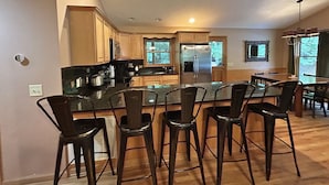 A modern kitchen with a central island, wooden cabinets, stainless steel appliances, and bar stools. - Dream on a Stream Log Cabin Lodge That Has It All! (Almond)