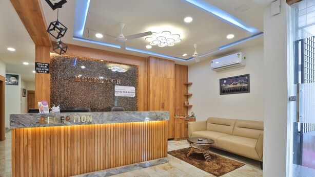 A hotel reception area with a marble counter, wooden paneling, a sofa, and a ceiling fan. - Hotel TGR Rooms (Palanpur)