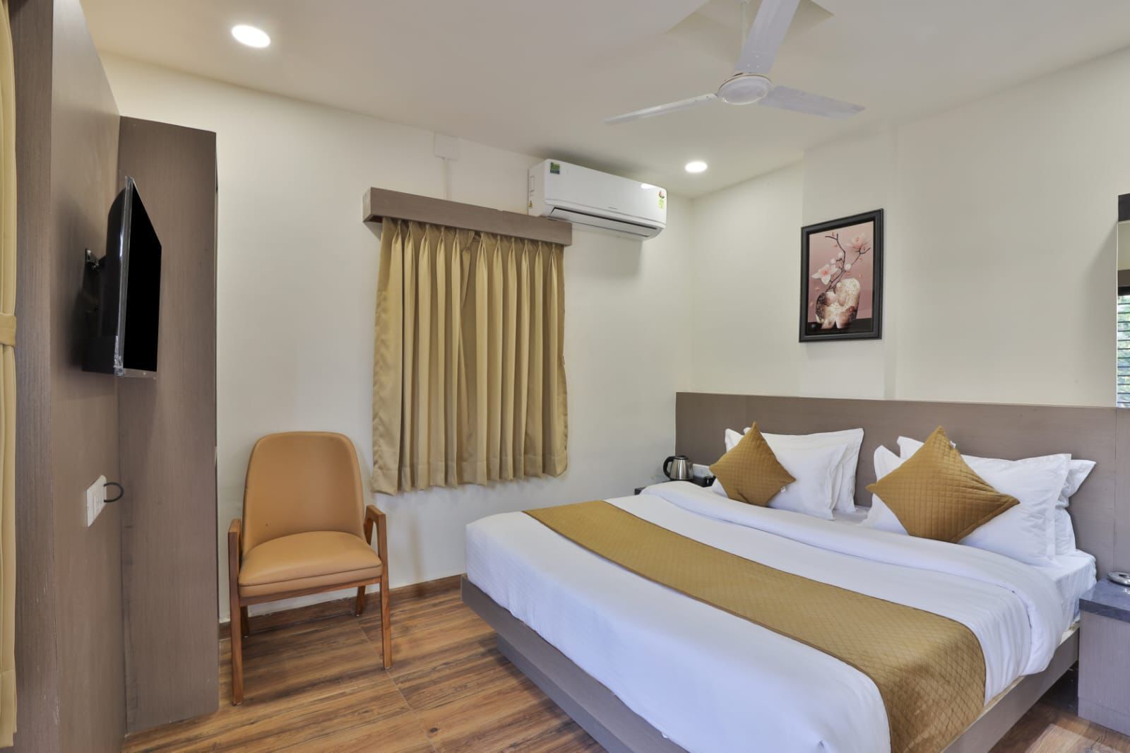A hotel room with a bed, a chair, a ceiling fan, an air conditioning unit, and a picture on the wall.