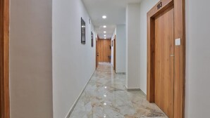 A hallway with marble flooring, wooden doors, and recessed ceiling lights. - Hotel TGR Rooms (Palanpur)