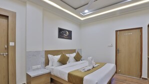 A hotel room with a bed, bedside tables, a nightstand, a wall-mounted artwork, and a door. - Hotel TGR Rooms (Palanpur)