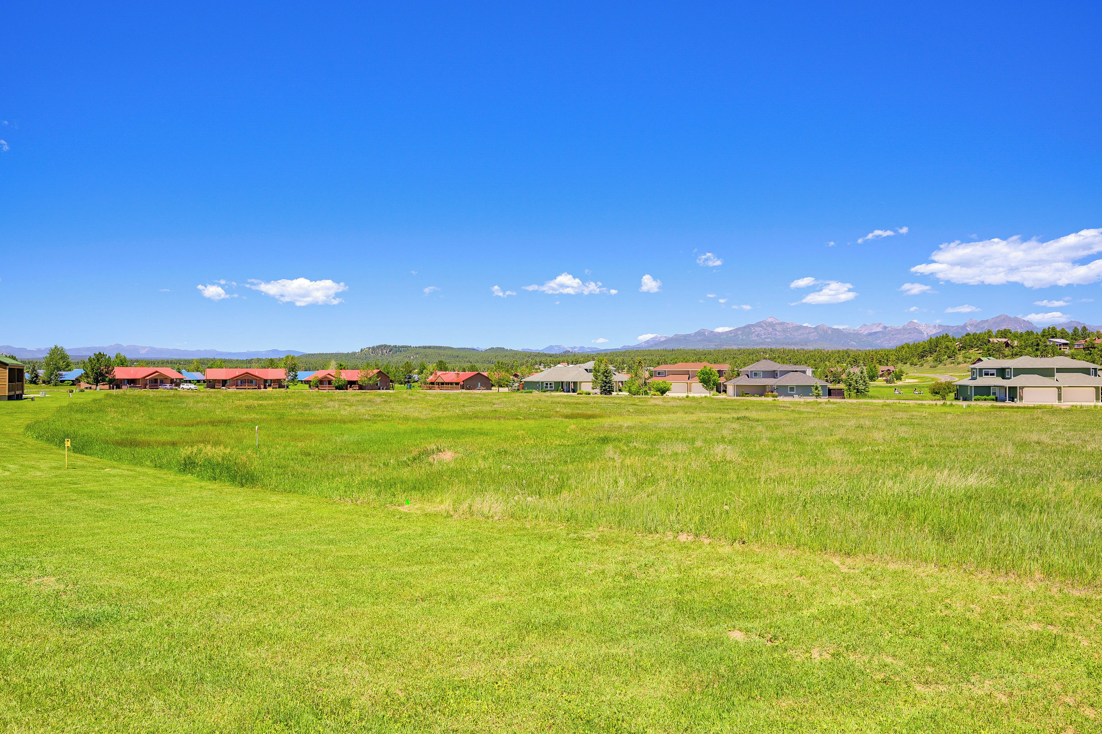 A grassy field with several houses in the background, some with red roofs.