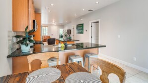 A modern kitchen with a central island, wooden cabinets, and a dining area with stools.