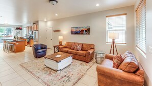 A spacious living room with a large brown leather sofa, a coffee table, and a dining area with a kitchen in the background.