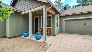 A house with a covered porch, two large potted plants, a brick driveway, and a garage.
