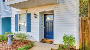A house with a front porch, a blue door, and a small garden area with a birdbath and plants. - Mobile Townhome Near University of South Alabama! (Mobile)