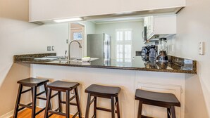 A kitchen with a granite countertop, three dark stools, a stainless steel refrigerator, and a large mirror above the counter. - Mobile Townhome Near University of South Alabama! (Mobile)