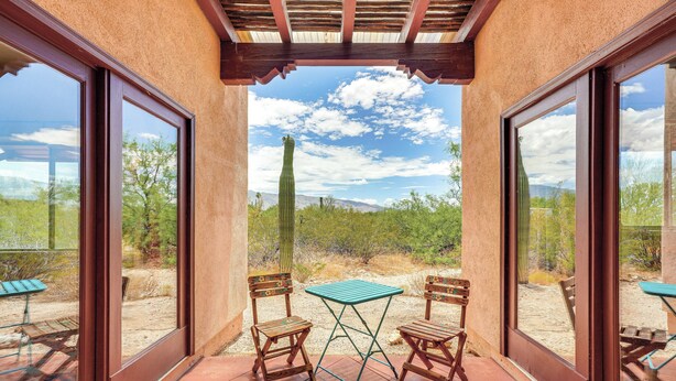 Une terrasse avec deux chaises en bois et une petite table, d’où l’on peut admirer un paysage désertique parsemé de cactus et dominé par des montagnes.