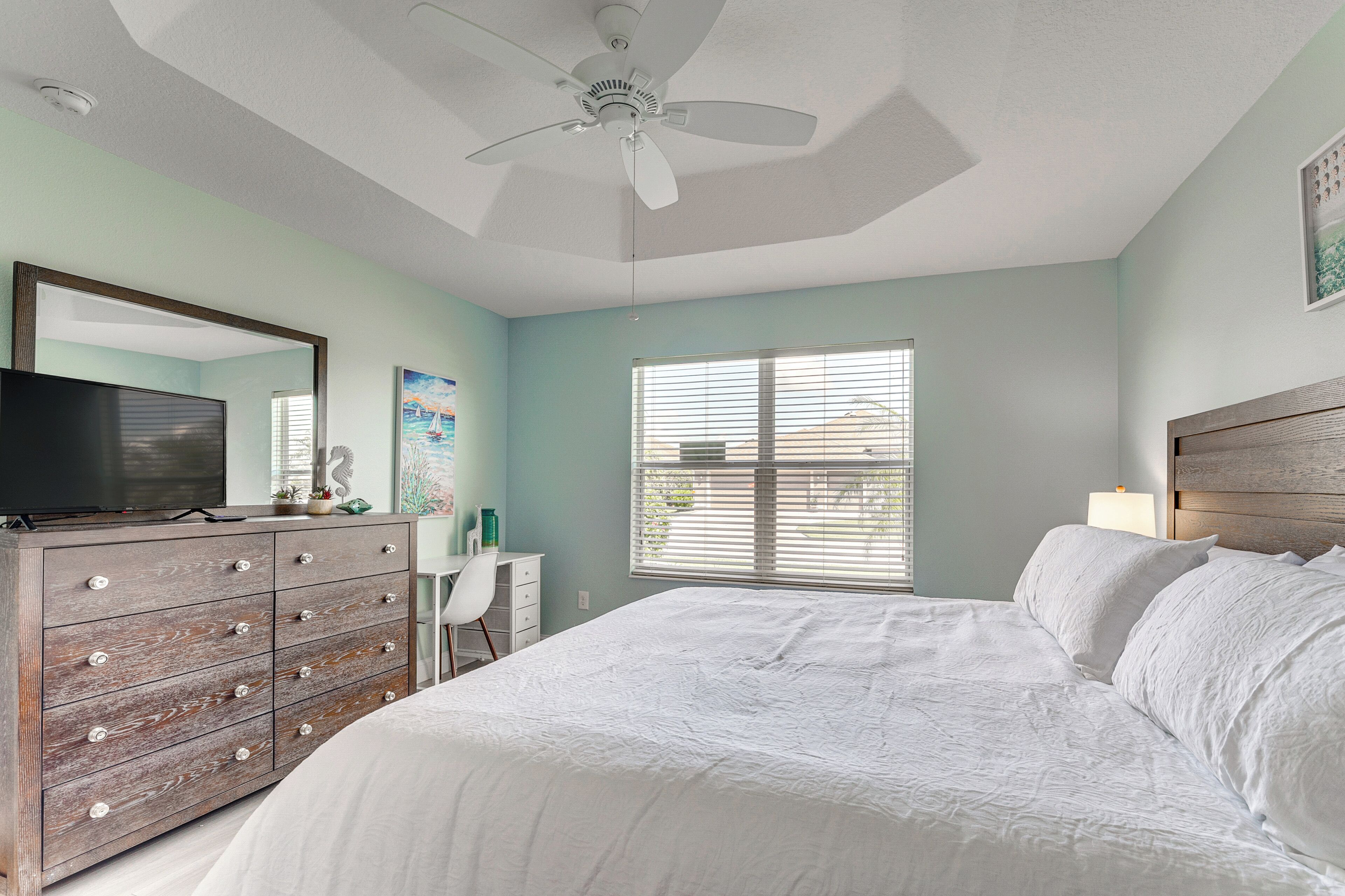 A bedroom with a bed, dresser, TV, and a ceiling fan.