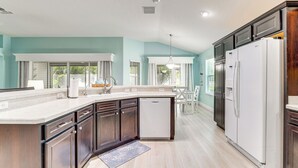 A modern kitchen with dark wood cabinets, a white refrigerator, and a large island with a dishwasher. - Golf Cart & Pool Access: The Villages Home! (Wildwood)