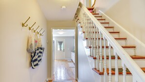 A hallway with a wooden staircase, a rug, and a door leading to another room.