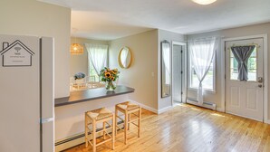 A kitchen with a refrigerator, two bar stools, a vase with flowers, and a hanging light fixture.