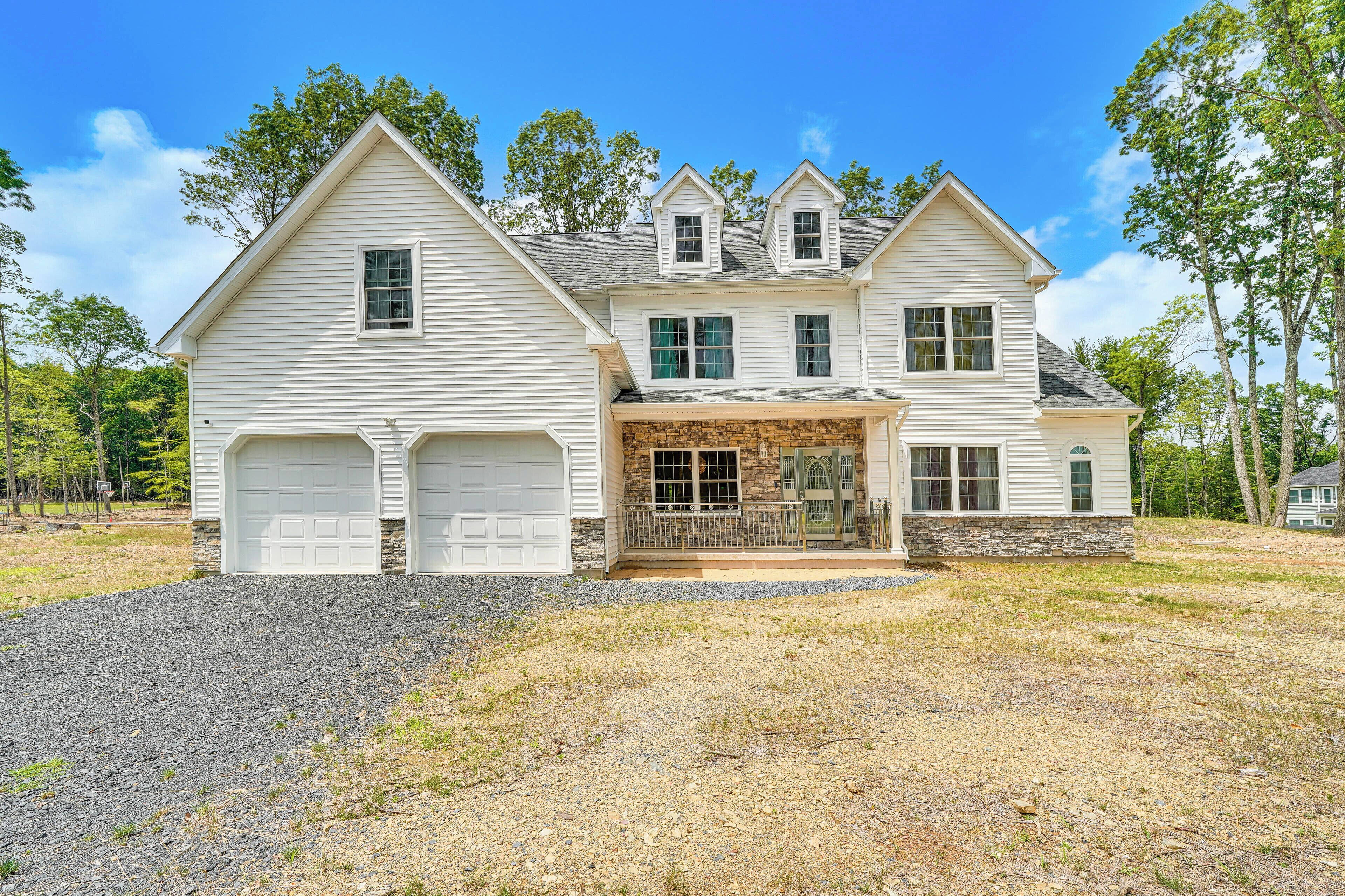 A two-story house with a garage, a stone foundation, and a front porch.