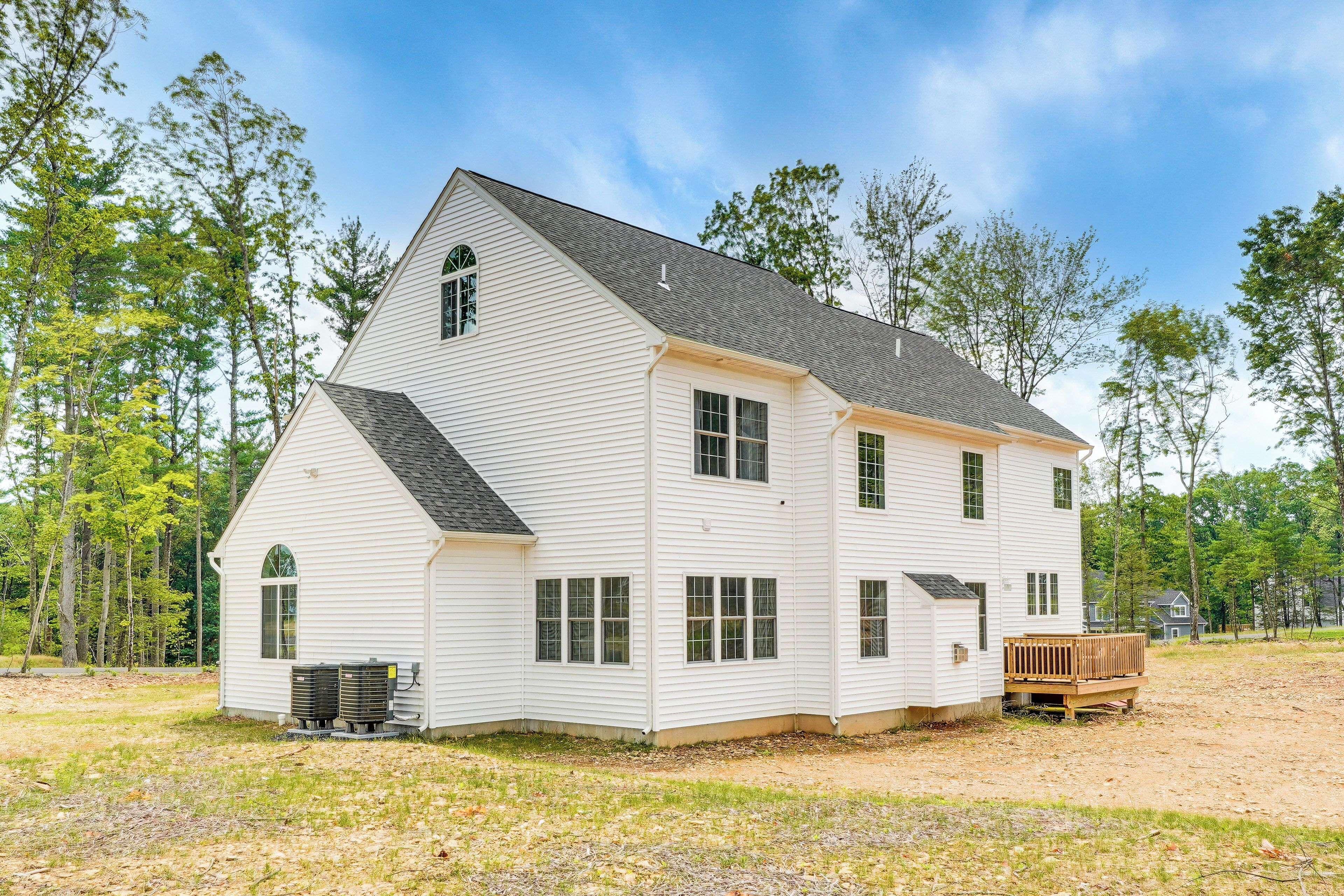 A large, single-story white house with a gabled roof, a wooden deck, and two air conditioning units in front.