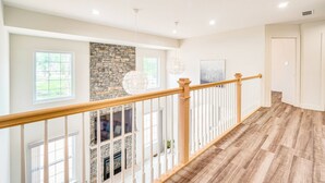A spacious interior with a wooden staircase, stone fireplace, and large windows. - Hike, Sip & Ski: Spacious Poconos Home (Kunkletown)