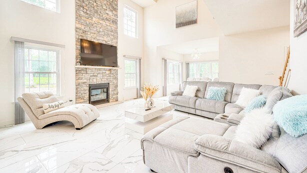 A spacious living room with a stone fireplace, a large sofa, and a TV mounted on the wall. - Hike, Sip & Ski: Spacious Poconos Home (Kunkletown)