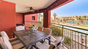 A balcony with a table and chairs, overlooking a pool and palm trees. - Riverfront Bullhead City Condo Near Casinos! (Bullhead City)