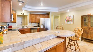 A kitchen with wooden cabinets, a stainless steel refrigerator, a dishwasher, and a dining area with a chair and table. - Riverfront Bullhead City Condo Near Casinos! (Bullhead City)