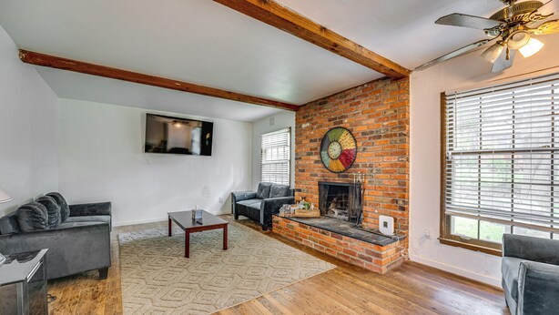 A living room with a fireplace, wooden floors, and a ceiling fan. - Spacious Southfield Home w/ Patio & Yard! (Southfield)