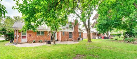 A brick house with a covered patio, surrounded by a well-maintained lawn and trees.