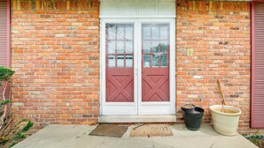 A brick building with a white door and red shutters, a doormat, and two potted plants. - Spacious Southfield Home w/ Patio & Yard! (Southfield)