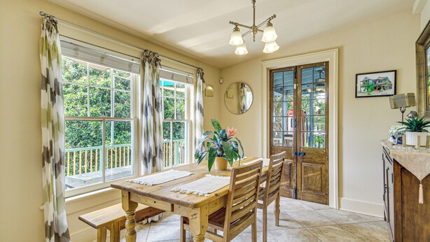 A dining area with a wooden table, chairs, and a potted plant. There are windows with curtains, a chandelier, and a mirror on the wall. - Eclectic Mandeville Home: Walk to Lakefront Park (Mandeville)
