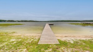 Un muelle de madera que se adentra en un lago tranquilo con aguas cristalinas y una orilla cubierta de hierba.