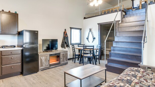 Una cocina compacta con electrodomésticos modernos, un comedor con mesa y sillas de madera, y una escalera que sube a un nivel superior.