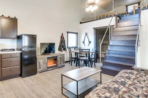 Una cucina compatta con elettrodomestici moderni, una zona pranzo con tavolo e sedie in legno, e una scala che conduce a un piano superiore.